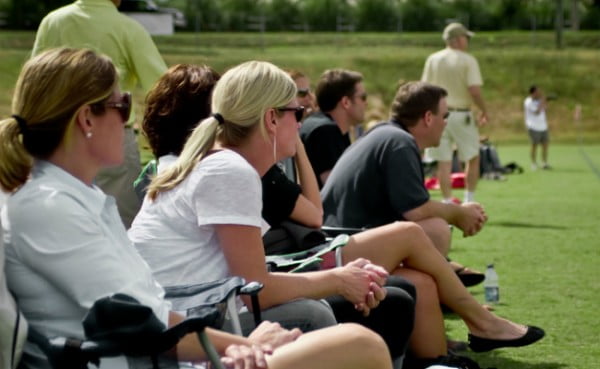 Parents watching youth soccer game from sideline, being critical of their kids' sports performance.